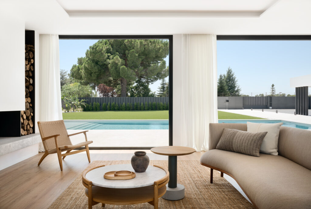 Interior de vivienda abierta al jardín con ventanales de suelo a techo que inundan el espacio de luz natural y bienestar.