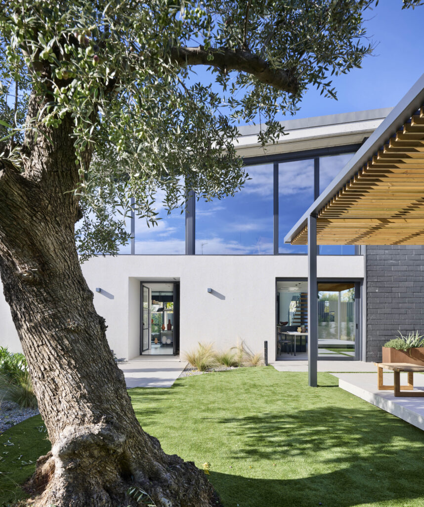 Diseño de espacios exteriores en vivienda con patio ajardinado y terraza cubierta, que conecta el interior con el jardín para el día a día.