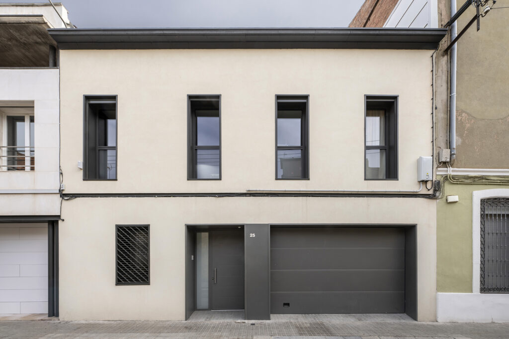 Fachada de vivienda urbana reformada con diseño contemporáneo, ventanas verticales alineadas y acceso integrado con puerta y garaje en planta baja.