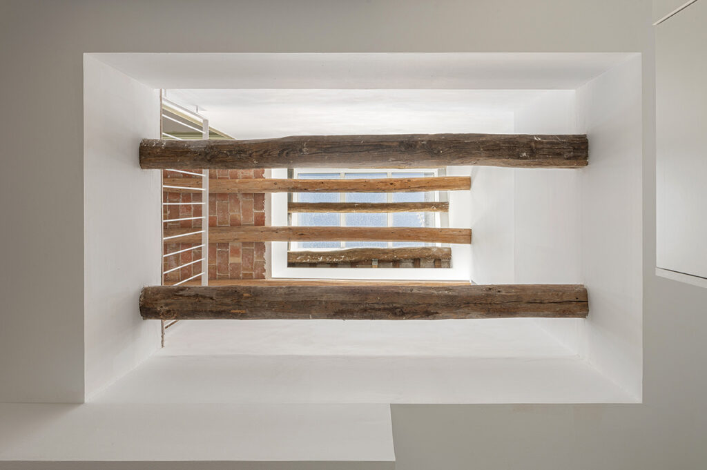 Entrada vertical de luz natural entre vigas de madera restauradas en una vivienda reformada con diseño arquitectónico contemporáneo.