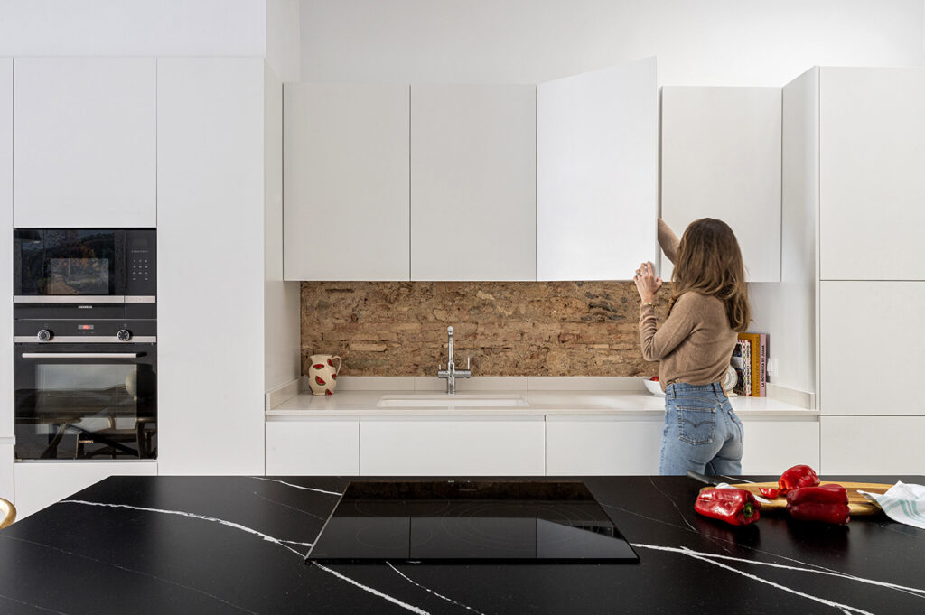 Tendencias de diseño 2026 en casa: cocina contemporánea con materiales honestos, muebles blancos y pared de ladrillo visto que aporta calidez y carácter.