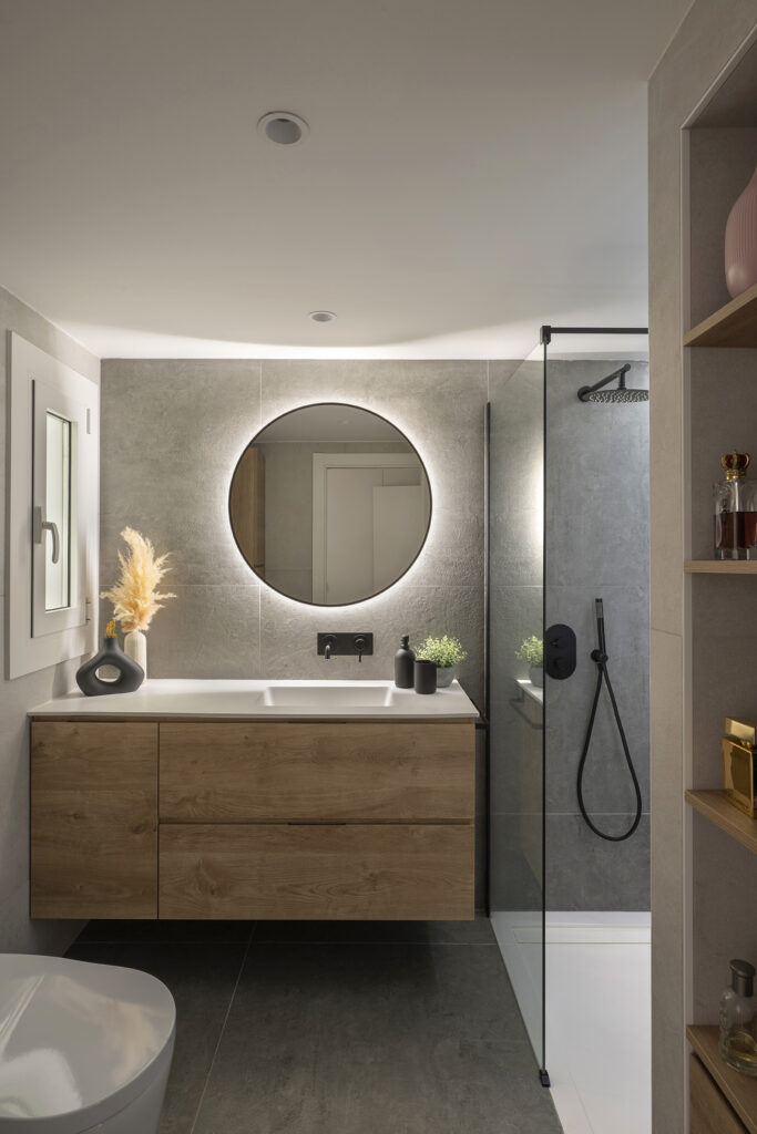 Baño cálido y práctico para el día a día, con mueble de madera, iluminación integrada y ducha accesible.