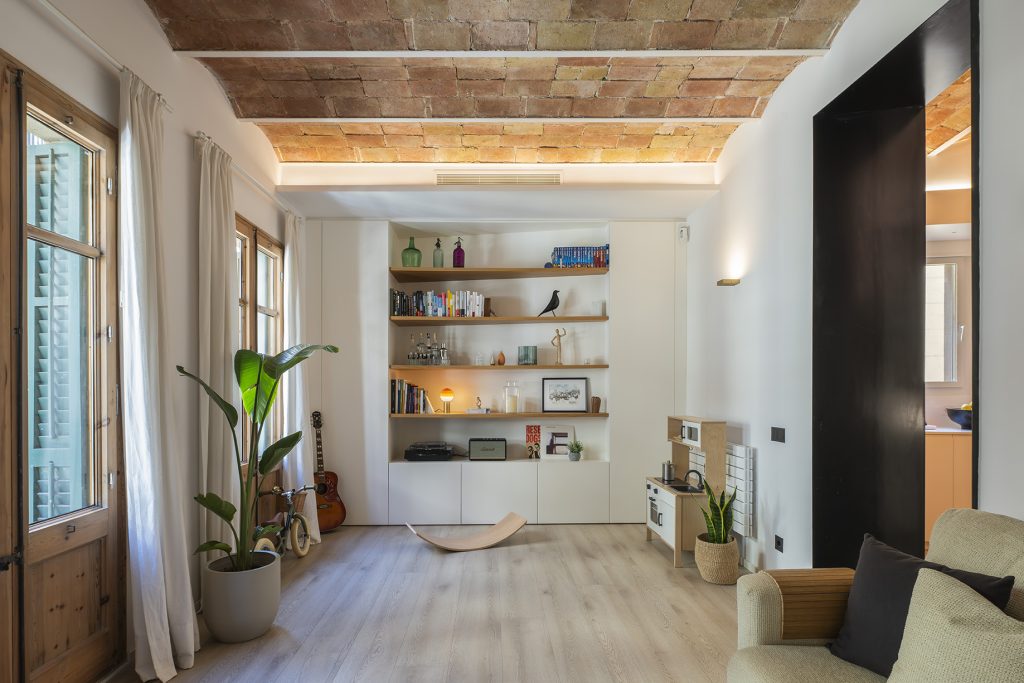 Salón reformado con diseño contemporáneo, bóveda catalana iluminada y estantería integrada que aporta calidez y funcionalidad al espacio.||||||